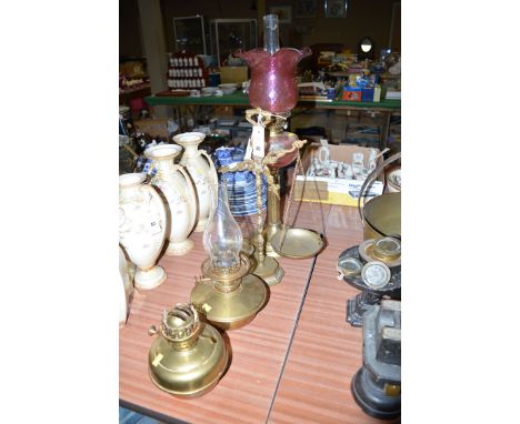 A Victorian table oil lamp with cranberry coloured damaged shade, coloured glass reservoir and raised on a brass column with 