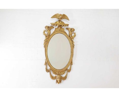 A giltwood oval wall mirror, late 19th/early 20th century, Northern European, with an eagle surmount and set with a pair of w