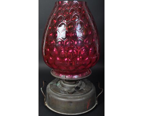 A vintage retro mid 20th century oil lamp having globular moulded cranberry glass shade over twin handled metal base. Measure