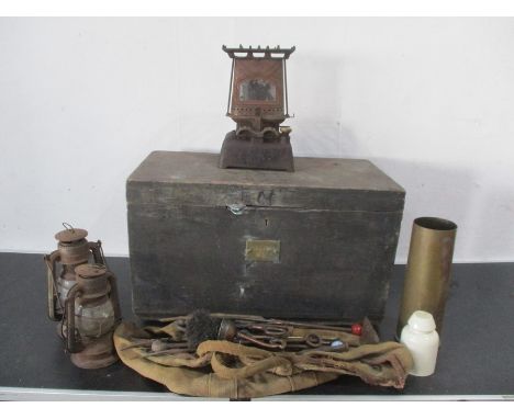 A wooden chest containing brass WWII shell, fireside tools, paraffin stove, storm lamps etc