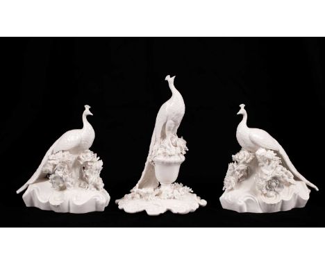 Two Coalport white glazed peacocks and a Royal Crown Derby example, modelled perched on flower-encrusted bases, all unmarked,