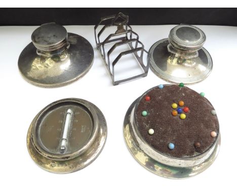 Two silver capstan inkwells, a pincushion, desk thermometer and a five bar toast rack (5) 