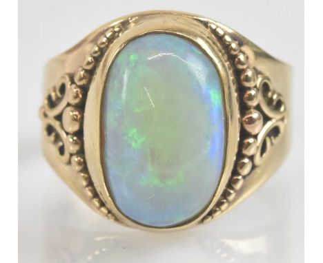 A vintage 9ct gold opal ring, the large oval opal showing flashes of blue and green, set in a bezel mount on a beaded collar 