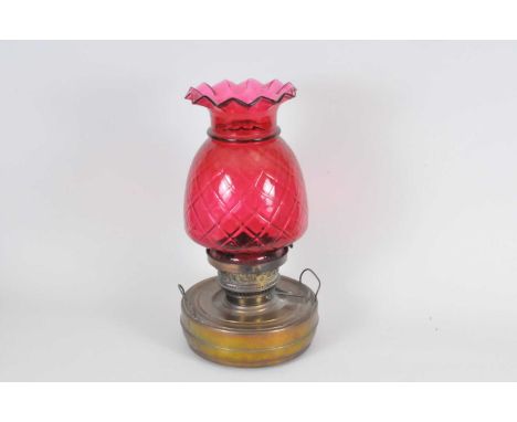 A large brass oil lamp, the cylindrical reservoir below a large pineapple-shaped cranberry glass shade, 50cm high combined.