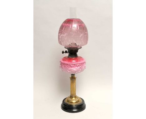 A Victorian oil lamp, with a fluted brass column supporting an opaque cranberry tinted glass resevoir, decorated with birds, 