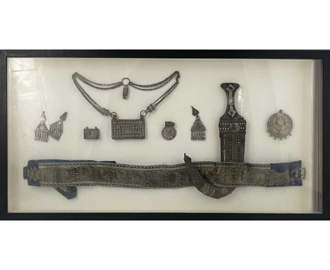 A framed display of Middle Eastern white metal mounted artifacts, including an Omani jambiya, embossed and filigree decoratio