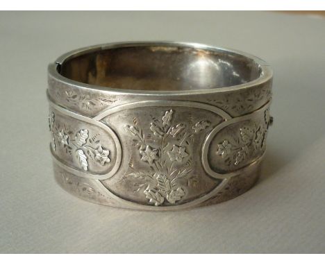 A Victorian silver hinged bangle, the face decorated with overlapping oval cartouches containing floral sprays, Birmingham, 1
