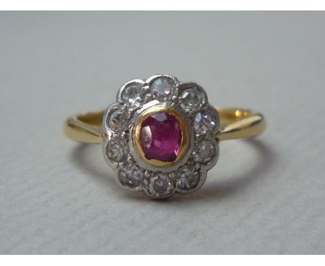 A ruby and diamond flowerhead cluster ring, the central oval stone of approximately 0.35ct rub-set, and surrounded by ten pla