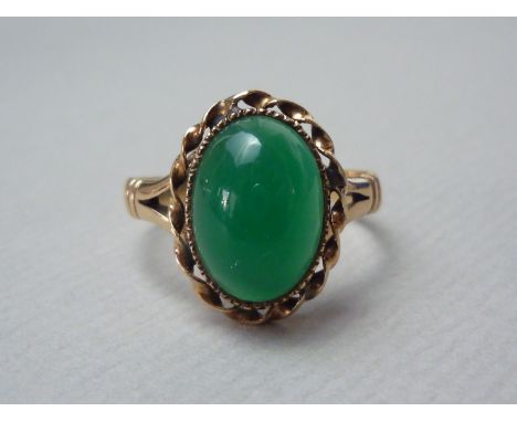 A jade cocktail ring, the cabochon stone of approximately 1.3 x 1 cm, rub and rope-twist set over a yellow-metal shank with b