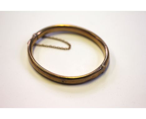 A 9ct yellow gold hinged, hollow bangle with attached safety chain, weight 8.9gms 