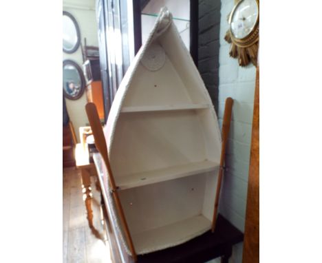 A pink and white painted boat shaped book shelf with oars 