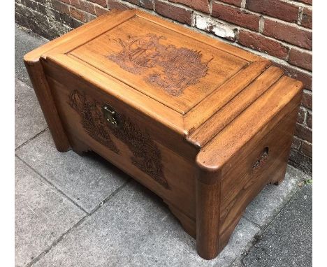 A large Chinese ornately carved camphor lined wood trunk, with scenes of ships and buildings, protruding rounded ends, raised