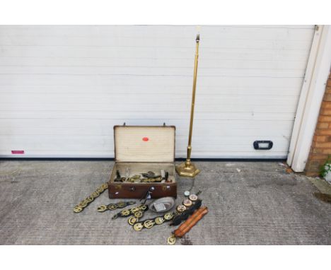 A vintage suitcase containing a quantity of various horse brasses, ships wheel nutcracker, brass inkwell, standard lamp and s
