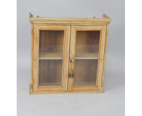 A pine wall mounted cupboard, with two glazed doors enclosing a single shelf, 79.5cm x 24.5cm x 80.5cm.