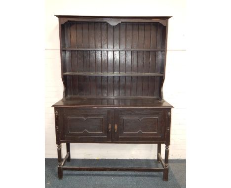 An oak dresser, the two shelf delft rack above cupboard doors, raised on turned legs united by stretchers, 137cm x 48cm x 194