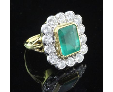 An unmarked gold, emerald and diamond cluster ring, the central emerald cut stone bordered with fourteen round brilliant cut 