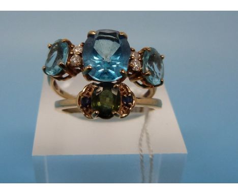 A 14k gold ring set with a central green sapphire flanked by two blue sapphires together with a 10k gold ring set with three 