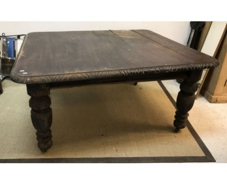 A late 19th Century oak dining table, the top with carved frieze, raised on heavily carved and turned legs to china castors, 