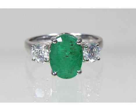 An impressive white gold emerald and diamond three stone ring, the central emerald flanked by a pair of diamonds, approximate