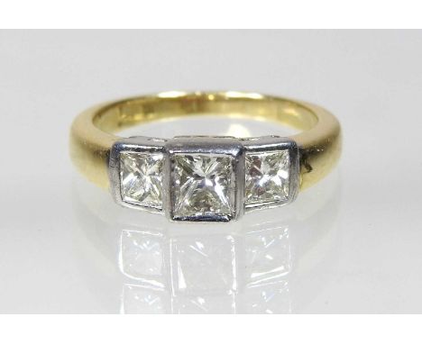 An 18 carat gold and platinum set princess cut three stone diamond ring, of stepped design, size J