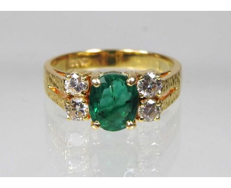 An 18 carat gold emerald and diamond ring, the central emerald flanked by four diamonds and having textured shoulders, approx