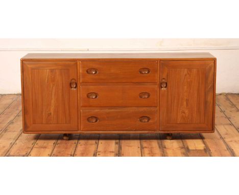 An Ercol blonde elm Windsor sideboard, model No. 455, having three central drawers flanked by cupboard doors, each with integ