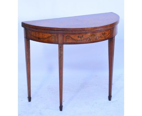 An Edwardian satinwood and inlaid demi-lune card table, the hinged top above floral decorated frieze and square section taper