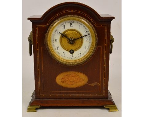 An Edwardian mahogany inlaid mantel clock, the enamel dial set with Arabic numerals, with brass lion handles to bracket feet,