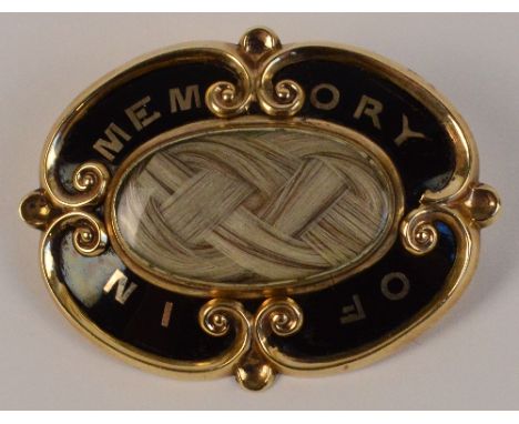 A Victorian yellow metal mourning brooch of oval shaped form centred with a glass hair aperture, inscribed "In memory of" on 