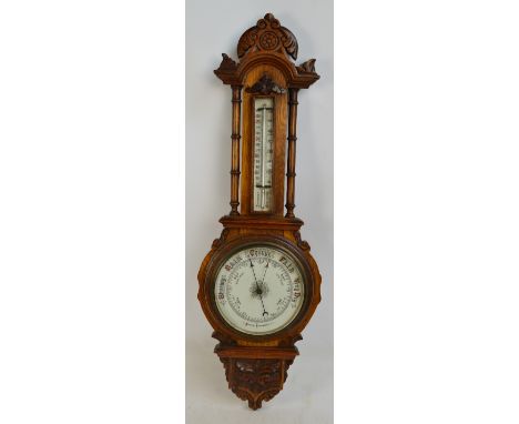 A late Victorian carved oak aneroid barometer with detailed case, thermometer above enameled barometer dial and floral carved