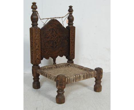 An early 20th Indian low carved hardwood chair having finial tops with a profusely carved backrest with foliate detailing ove