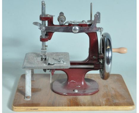 A vintage 1950s hand operated mini sewing machine for girls having a burgundy colourway raised on a square wooden platform wi