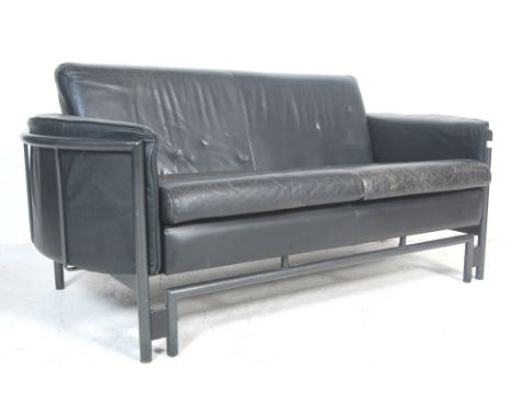 A vintage late 20th century two seater black leather sofa / settee having curved armrests, detachable cushions, cylindrical t