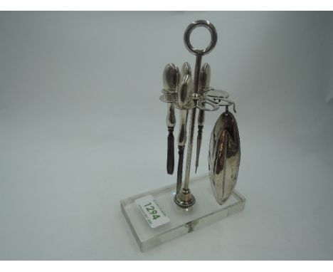 A white metal dressing table manicure stand having five HM silver handled manicure tools to white metal stand on a glass base