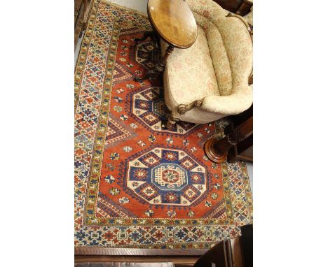 20th Century Turkish carpet of Kazak design with a triple hooked medallion pattern on a terracotta ground with borders, 118in