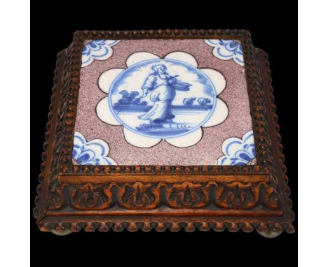 A Delft polychrome pottery tile depicting a farmer's wife, in carved wood stand with brass feet, stand width 18cm Good condit