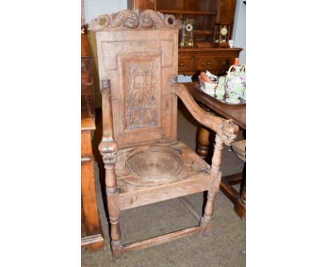 An 18th century carved oak commode chair (alterations), the back panel carved with interior scenes 