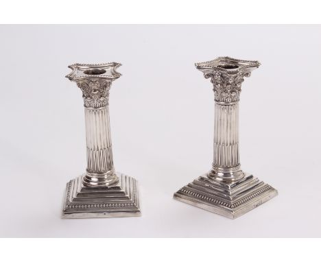 A pair of late Victorian silver filled candlesticks by Edward Hutton, having square bases supporting corinthium columns, date