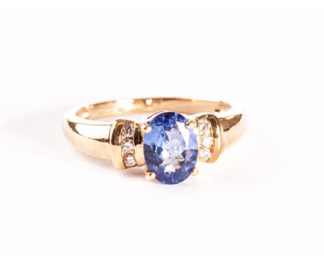 A modern 18ct gold and gem set ring, the central oval blue stone, possibly a tanzinite, flanked by a column of three brillian