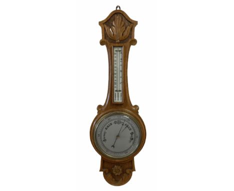 An English 1930�s solid oak carved hall barometer in a scroll shaped carved case with applied floral and leaf carving, compen