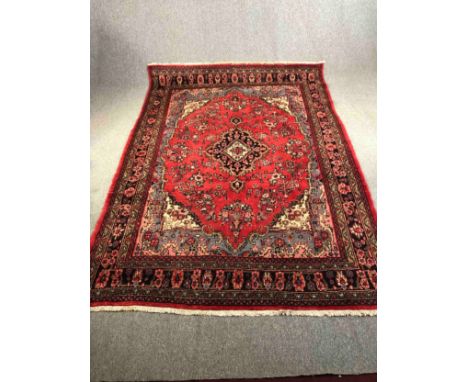 A Persian Sarouk carpet with central medallion and flowerhead motifs across the burgundy field within foliate multiple border