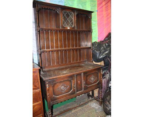 A reproduction Oak Jacobean style Dresser, having moulded cornice to the plate rack with central leaded glazed single door, b