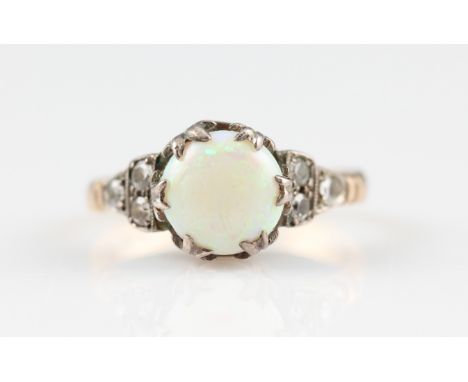 An opal ring, set with a circular opal cabochon, measuring approx. 8mm, flanked to either side with three colourless pastes, 