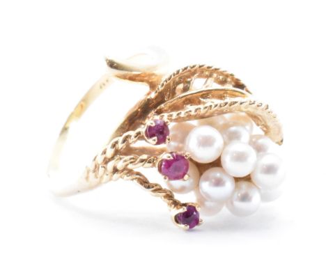 A 14ct gold ruby and diamond dress ring. The floral ring having a cluster of pearls and three prong set rubies. Ring size K /