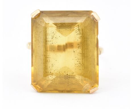 A 9ct gold and citrine dress ring. The ring set with a large emerald cut citrinein a four pronged setting having serpentine d