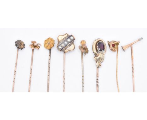 A collection of gold and yellow metal stick pins. The pins to include a hunting horn pin, a Victorian garnet set pin, a shamr