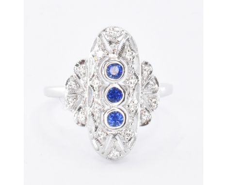 A silver Art Deco style panel ring set with three round cut synthetic sapphires surrounded by a halo of CZ's. Marked sterling