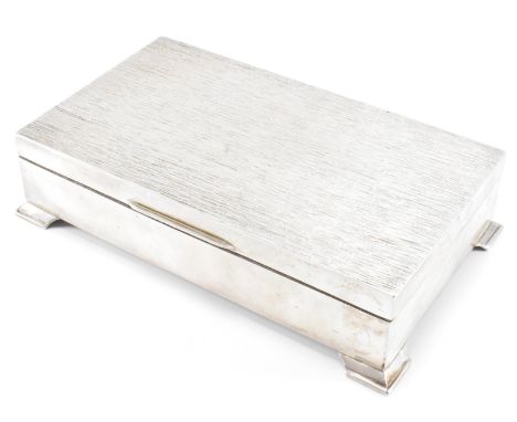 A silver hallmarked desk top cigarette box. The box of rectangular form having a bark effect lid with bracket feet. Hallmarke