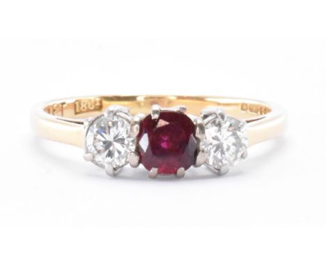 A hallmarked 18ct gold three stone ring. The ring set with a central round cut ruby flanked by two round cut diamonds in pron