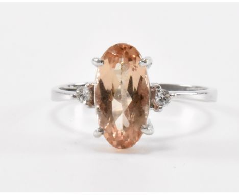 An 18ct white gold and orange topaz ring set with an oval cut topaz flanked by two round cut diamonds. Marked 750 to the inte